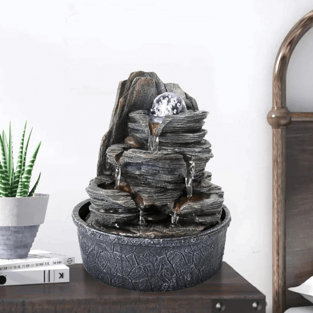 A tabletop fountain featuring water flowing over stacked stone-like tiers with a glass orb at the top